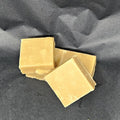 Three square pieces of yellow vanilla Soft Fudge on a dark gray background