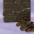 Dark chocolate bar with raisins on a light purple background